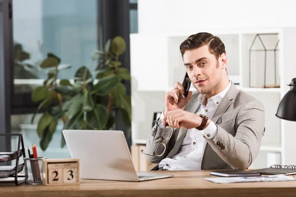 Schöner Geschäftsmann telefoniert am Arbeitsplatz im Büro und schaut in die Kamera — Stockfoto