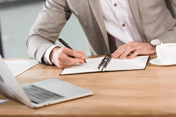 Tiro recortado do homem de negócios que escreve no caderno no local de trabalho — Fotografia de Stock