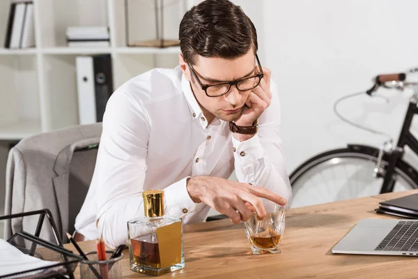 Homme d'affaires déprimé avec un verre de whisky assis sur le lieu de travail au bureau — Photo de stock