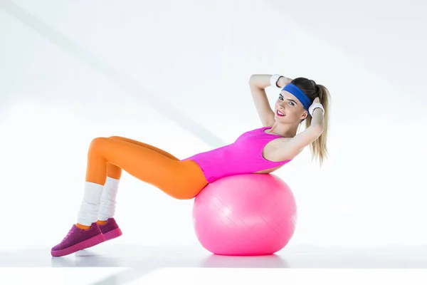 Sportliche junge Frau macht Bauch auf fittem Ball und lächelt in die Kamera auf grau — Stockfoto