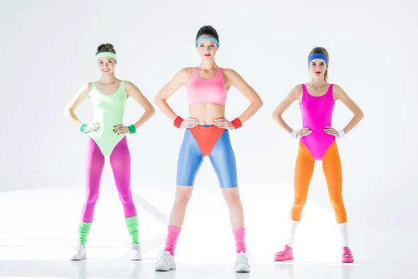 Full length view of beautiful sporty girls standing with hands on waist and smiling at camera on grey — Stock Photo