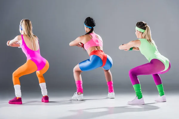 Rear view of sporty young women doing squat together on grey — Stock Photo