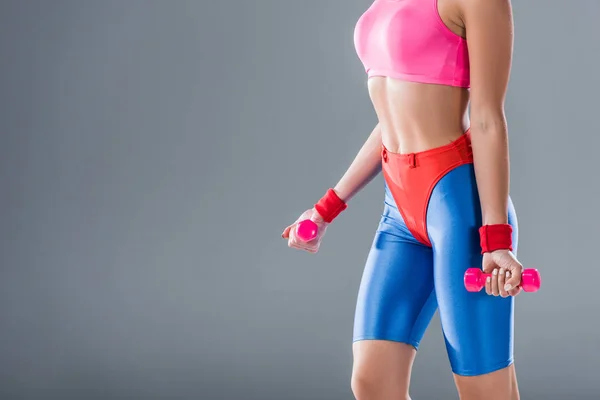Обрезанный снимок спортивной девушки, тренирующейся с гантелями, изолированными на сером — стоковое фото