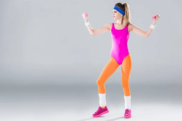 Vue complète de la jeune femme sportive faisant de l'exercice avec des haltères sur gris — Photo de stock