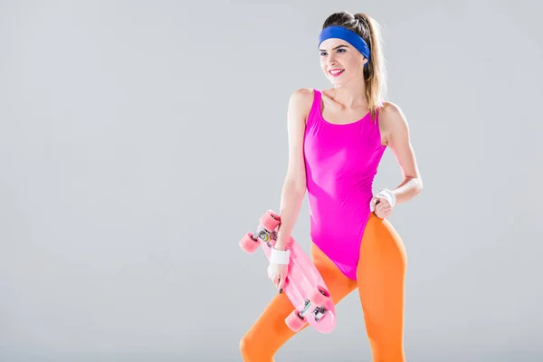 Sonriente joven deportista sosteniendo penny board y mirando hacia otro lado aislado en gris - foto de stock