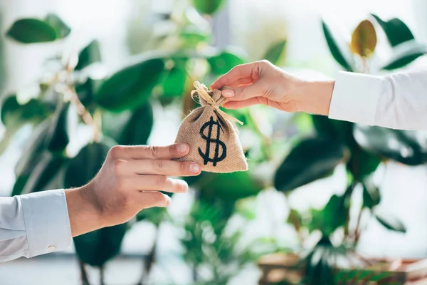 Partial view of people holding sackcloth bag with dollar sign in hands — Stock Photo