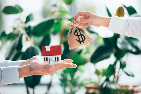 Partial view of people exchanging sackcloth bag with dollar sign and house model — Stock Photo