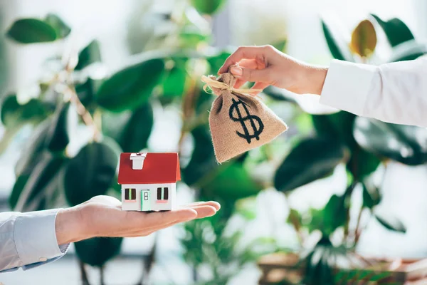 Cropped shot of people exchanging sackcloth bag with dollar sign and house model — Stock Photo