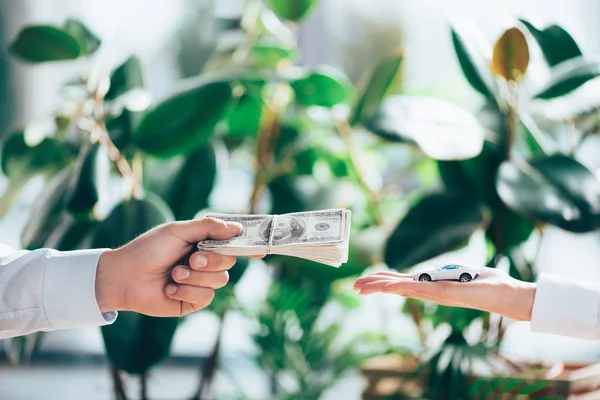 Tiro recortado de personas que intercambian billetes de dólar y modelo de coche - foto de stock