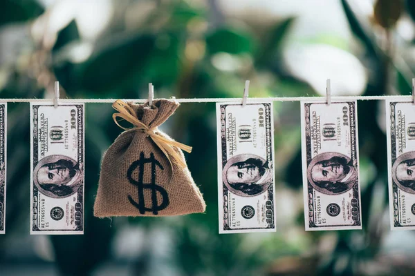 Sackcloth bag with dollar sign and dollar banknotes hanging on rope — Stock Photo