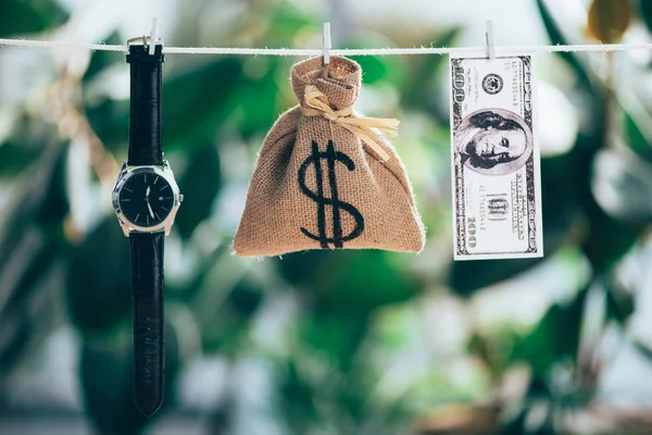 Saco de pano de saco, relógio de pulso e nota de dólar pendurada na corda — Fotografia de Stock