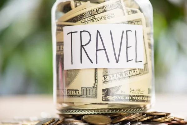 Pile of coins, glass jar with dollar banknotes and inscription travel — Stock Photo