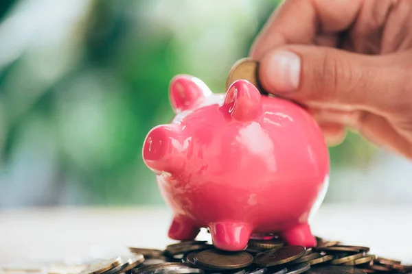 Close-up partial view of person putting coin into pink piggy bank — Stock Photo