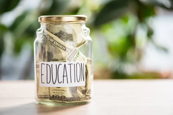 Close-up view of glass jar with dollar banknotes and inscription education — Stock Photo