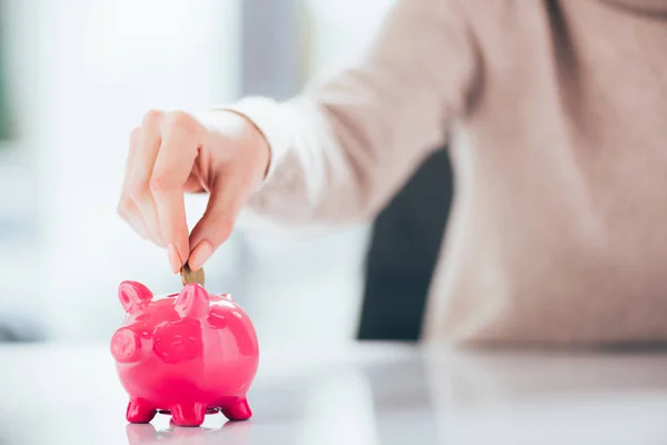 Close-up partial view of woman putting coin into pink piggy bank — Stock Photo