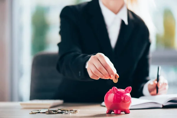 Partial view of businesswoman putting coin into pink piggy bank — Stock Photo