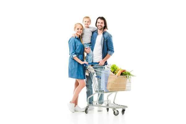 Feliz família abraçando uns aos outros e segurando carrinho de compras com sacos de supermercado isolados em branco — Fotografia de Stock