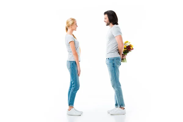 Paar bleibt und schaut einander an, Mann versteckt Blumenstrauß auf weißem Grund — Stockfoto