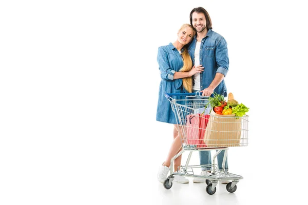 Happy couple with shopping cart full of bags looking at camera isolated on white — Stock Photo