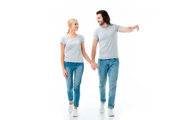 Hermosa pareja sonriente cogida de la mano mientras el hombre señala algo aislado en blanco - foto de stock