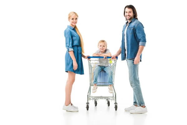 Bella famiglia sorridente alla fotocamera mentre il bambino seduto nel carrello della spesa isolato su bianco — Foto stock
