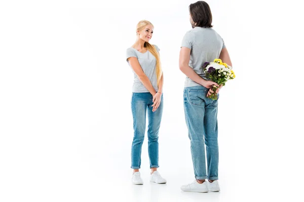 Casal maravilhoso olhando um para o outro, homem segurando flores atrás das costas isolado no branco — Fotografia de Stock