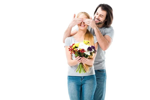Удивительная женщина держит цветы, в то время как мужчина закрывает глаза, чтобы сделать сюрприз, изолированные на белом — стоковое фото
