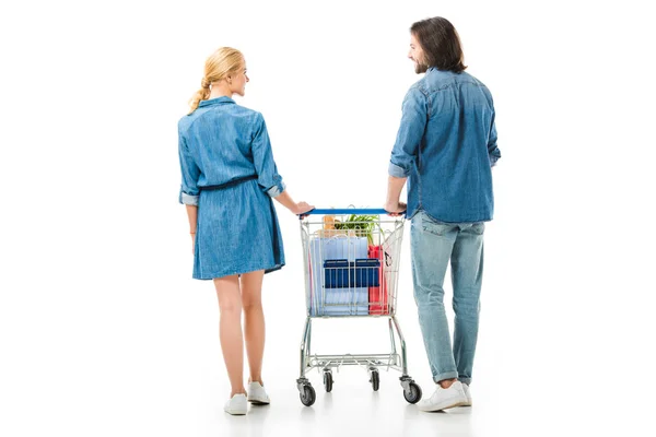 Visão traseira do casal segurando carrinho de compras com sacos isolados em branco — Fotografia de Stock