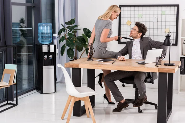 Jovem empresária puxando colegas amarrar enquanto sentado na mesa no escritório, conceito de romance de escritório — Fotografia de Stock