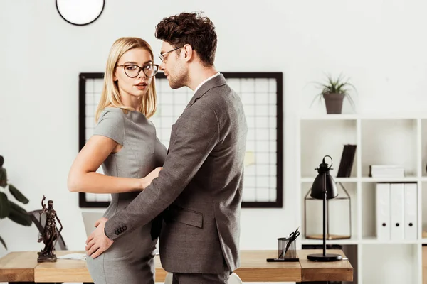 Young lawyers hugging each other while standing in office, flirt and office romance concept — Stock Photo