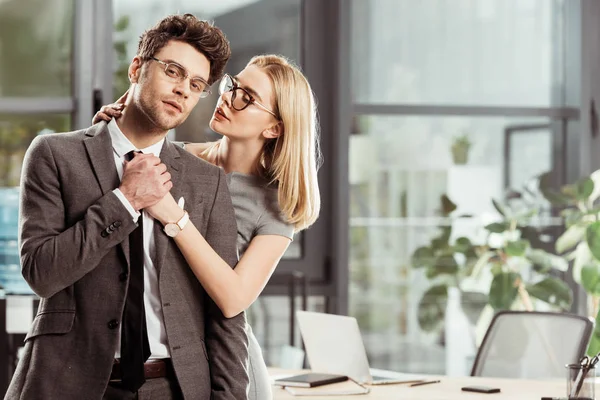 Beautiful businesswoman hugging stylish businessman in office, flirt and office romance concept — Stock Photo