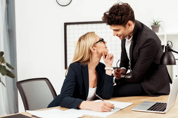 Side view of young businesspeople looking at each other at workplace, flirting and office romance concept — Stock Photo