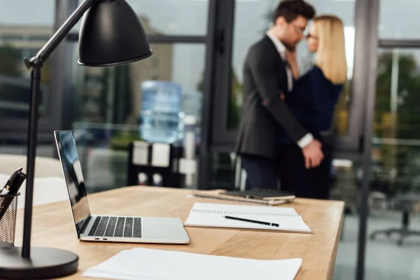 Foyer sélectif du lieu de travail avec ordinateur portable et hommes d'affaires étreignant derrière dans le bureau, concept de romance de bureau — Photo de stock