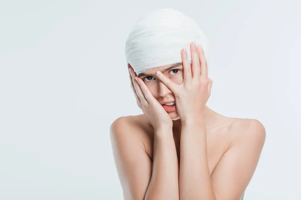 Femme nue avec des bandages blancs et les mains sur le visage isolé sur blanc — Photo de stock