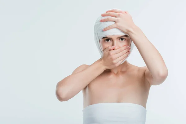 Woman with white bandages on head closing mouth with hand isolated on white — Stock Photo