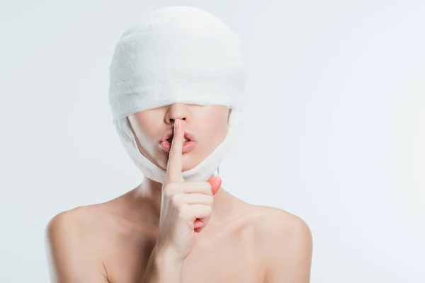 Gros plan de la femme en bandages blancs sur la tête montrant un signe de silence isolé sur blanc — Photo de stock