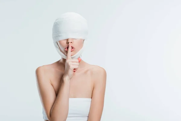 Mujer con vendajes blancos en la cabeza mostrando un signo de silencio aislado en blanco - foto de stock