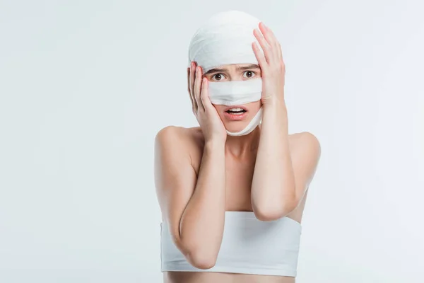Mulher assustada com bandagens segurando a cabeça isolada no branco — Fotografia de Stock