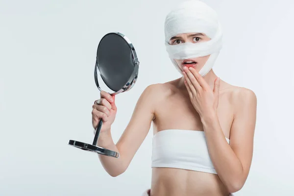 Mulher assustada com bandagens segurando espelho isolado no branco — Fotografia de Stock