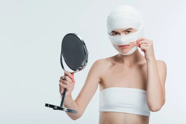 Upset woman with bandages and mirror touching cheek isolated on white — Stock Photo