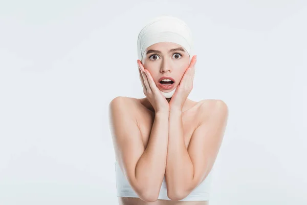 Mujer asustada con vendajes sobre la cabeza después de una cirugía plástica aislada en blanco - foto de stock