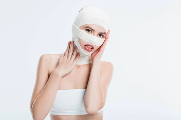 Femme avec des bandages après une chirurgie plastique touchant la tête isolé sur blanc — Photo de stock