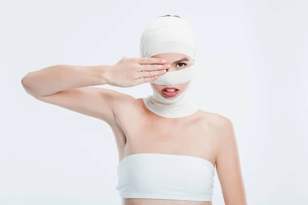 Mujer con vendajes después de la cirugía plástica ocultando el ojo detrás de la mano aislado en blanco — Stock Photo
