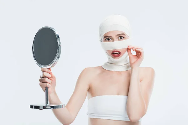 Donna spaventata con bende sopra la testa tenendo specchio isolato su bianco — Foto stock