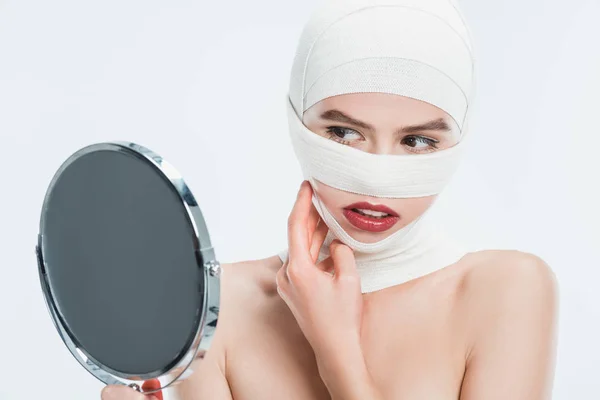 Primer plano de la mujer con vendajes sobre la cabeza mirando el espejo aislado en blanco - foto de stock