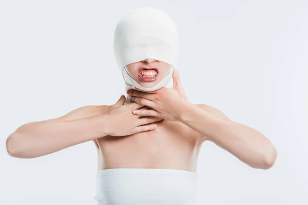 Сердита жінка з бинтами на голові після пластичної хірургії, торкаючись горла, ізольована на білому — стокове фото