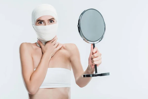 Femme effrayée après la chirurgie plastique sur le visage regardant miroir isolé sur blanc — Photo de stock