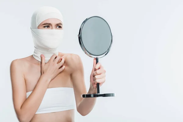 Verängstigte Frau nach Schönheitsoperation im Gesicht mit Blick auf Spiegel isoliert auf Weiß — Stockfoto