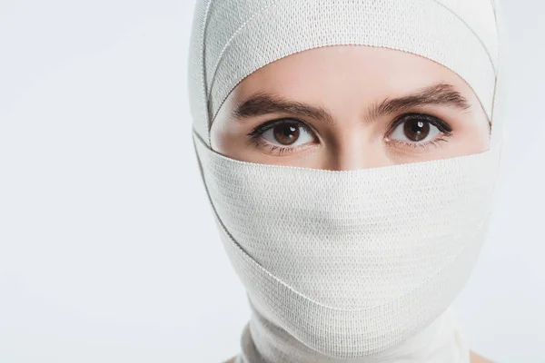 Mujer con vendajes blancos sobre la cara y la cabeza mirando a la cámara aislada en blanco - foto de stock