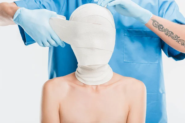 Primer plano del cirujano plástico en guantes que tapan la cara de la mujer con vendaje aislado en blanco - foto de stock